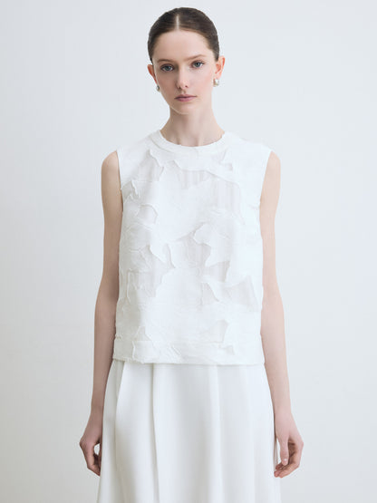 Woman wearing a floral white sleeveless top with floral details on a plain background