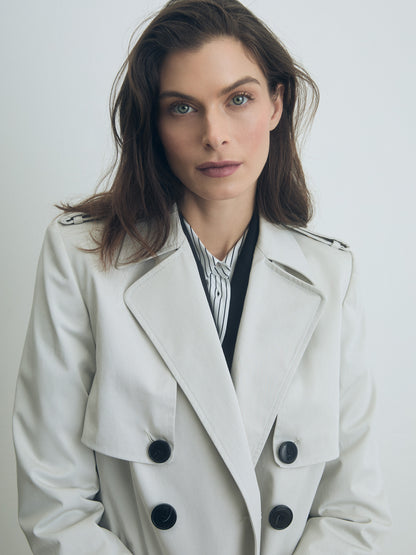 Woman wearing a pearl belted trench coat with black buttons against a plain background