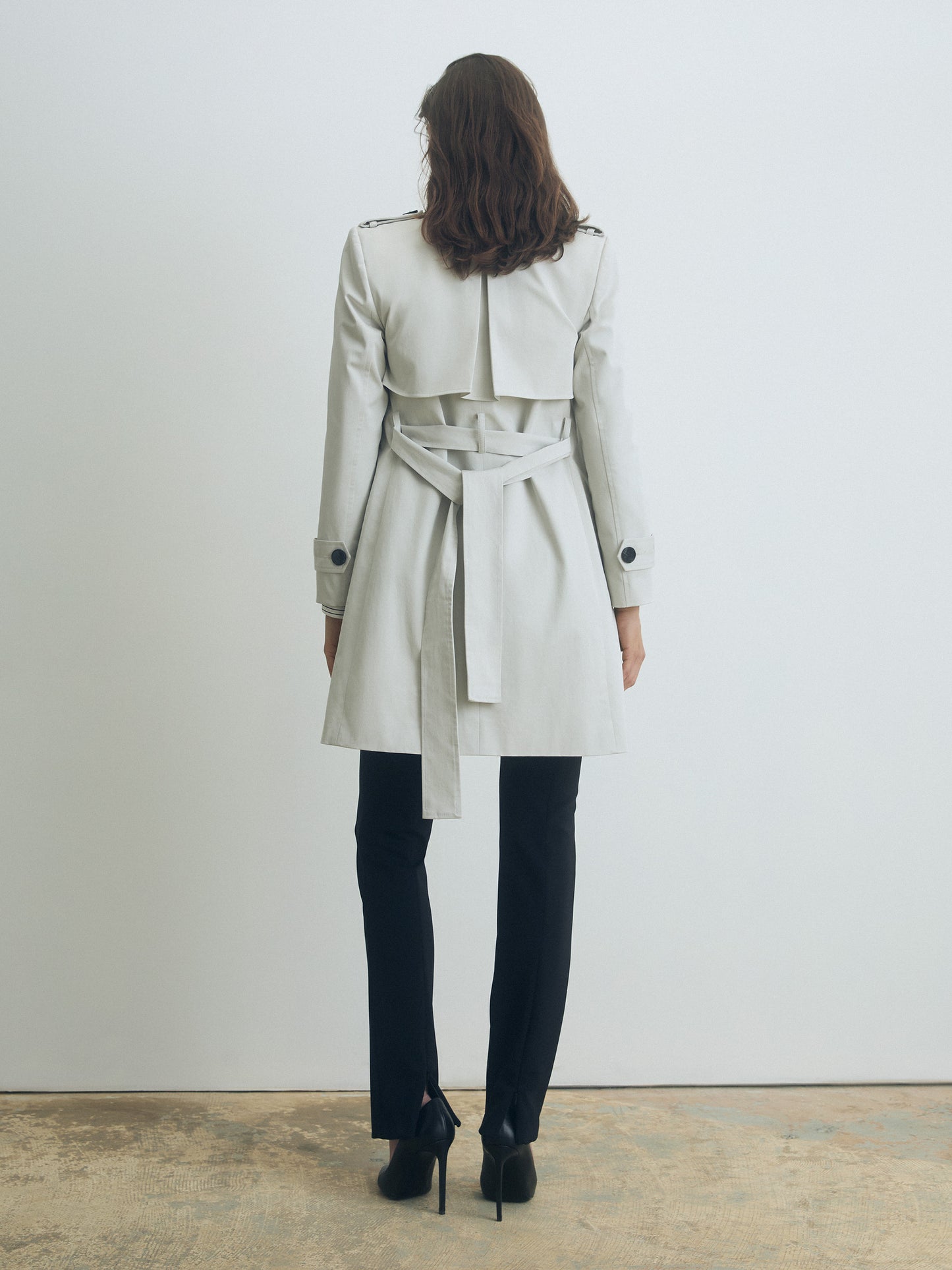 Person wearing a pearl trench coat with a belt, standing against a plain white wall.