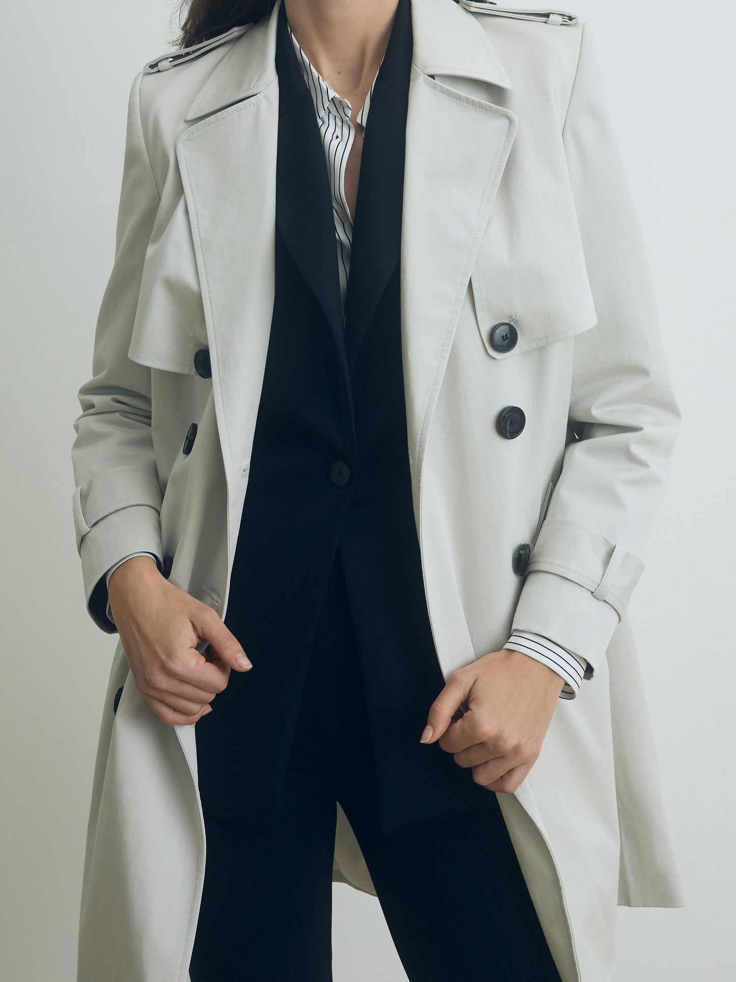 Person wearing a pearl coat over a dark suit and striped shirt on a plain background