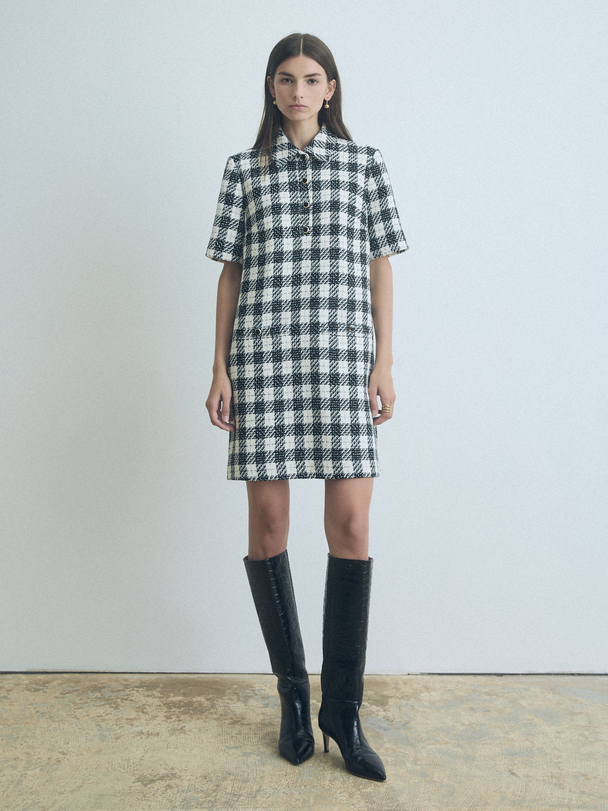 Woman wearing a black and white judith and charles checkered dress with knee-high black boots against a plain background