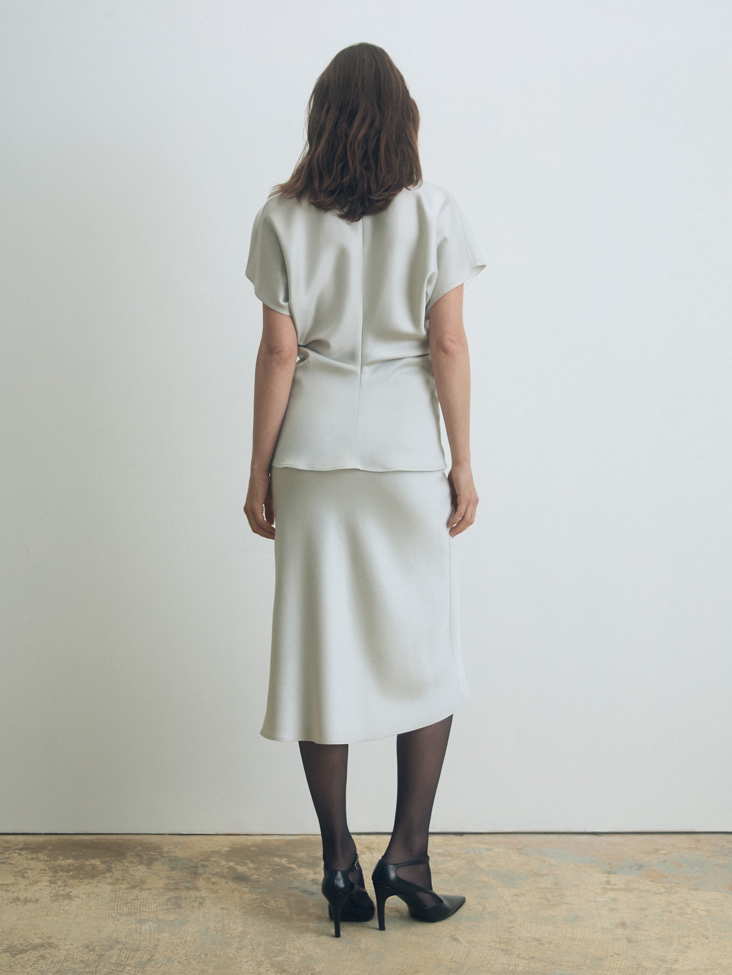 Woman wearing a pearl outfit standing against a plain white wall.
