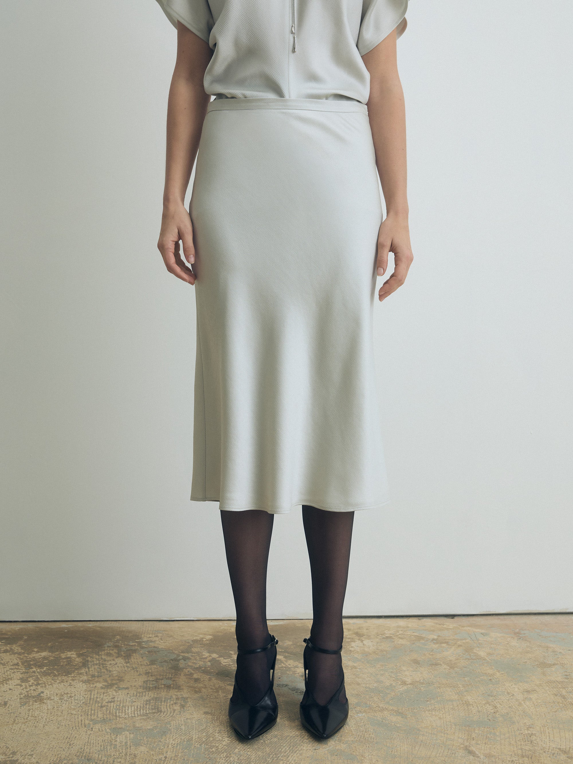 Person wearing a light-colored pearl skirt and top against a plain background