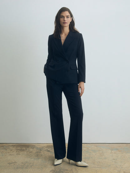 Woman wearing a navy blue suit standing against a plain background