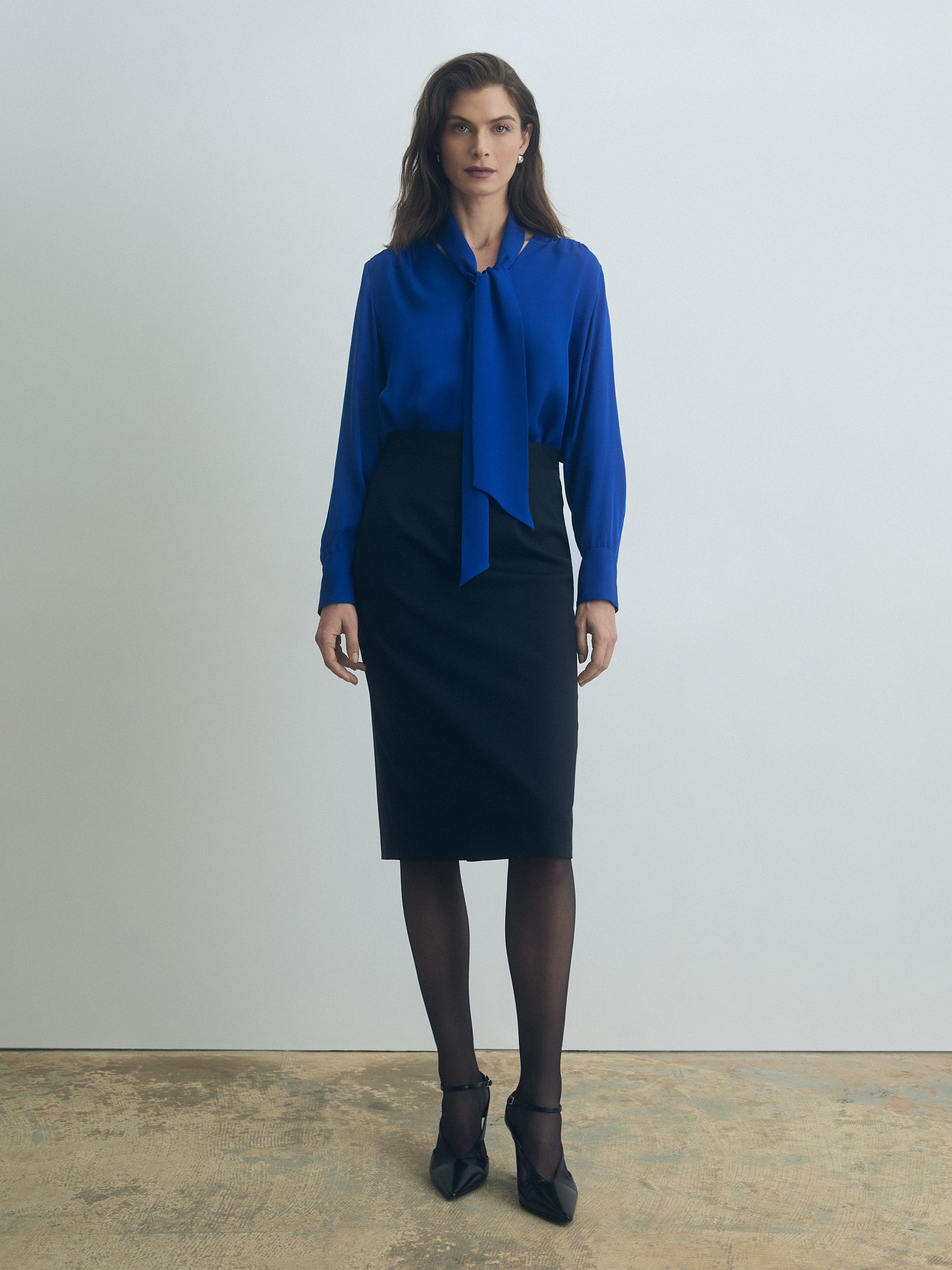 Woman wearing a blue ocean cavaiiere blouse and navy skirt against a plain background