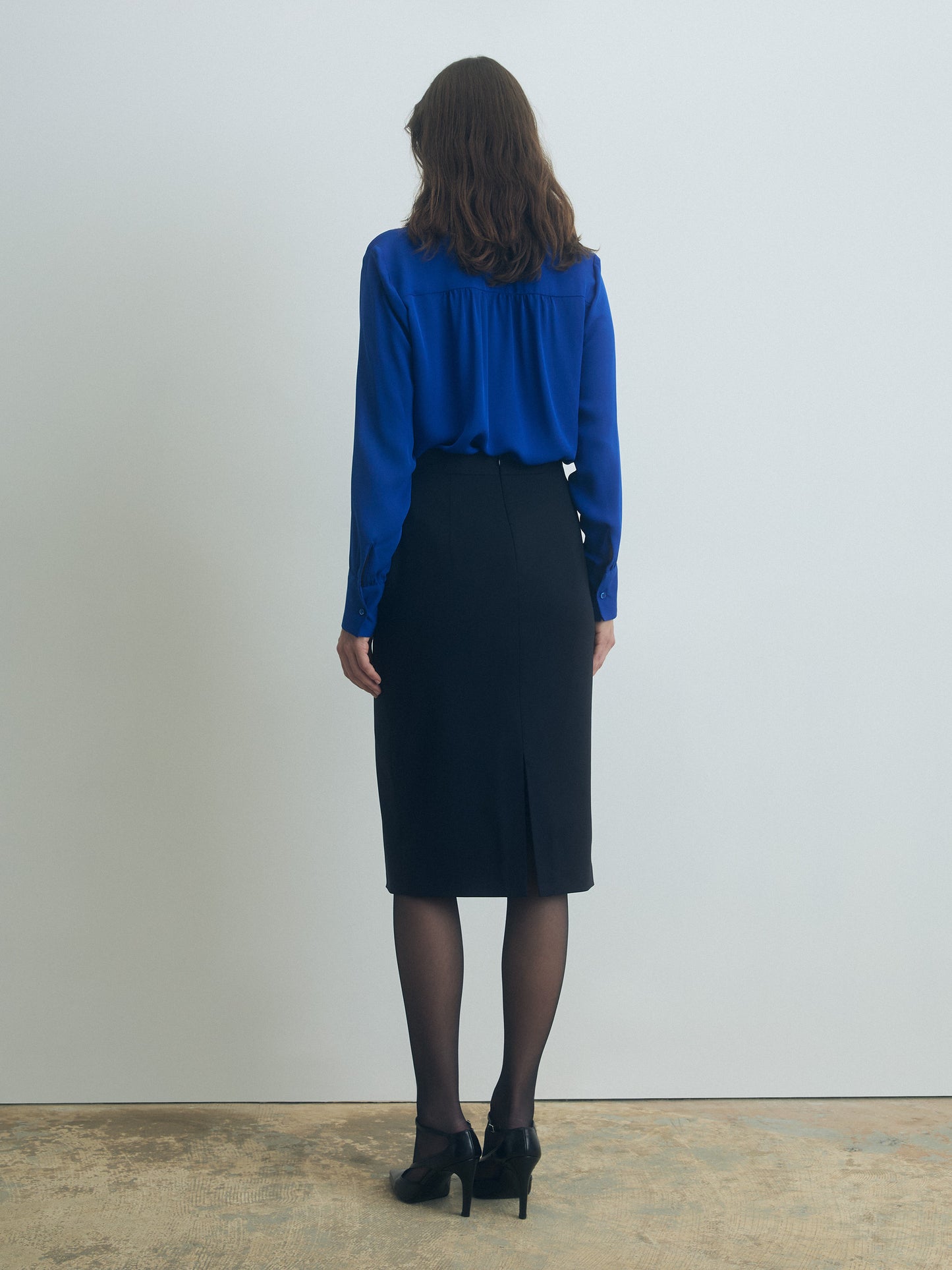 Person wearing an ocean blue blouse and navy skirt against a plain background