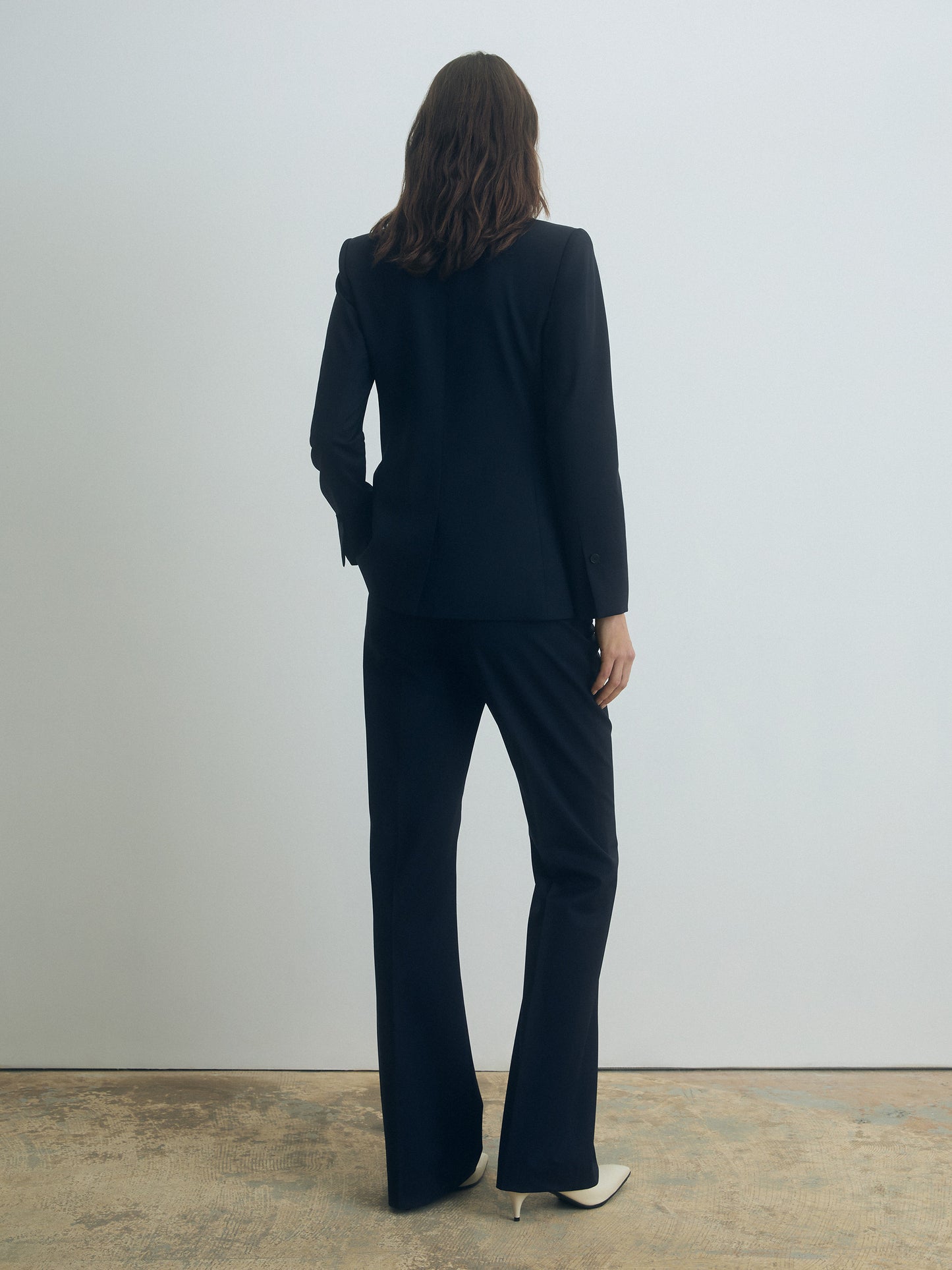 Woman wearing a navy suit standing against a plain white wall.