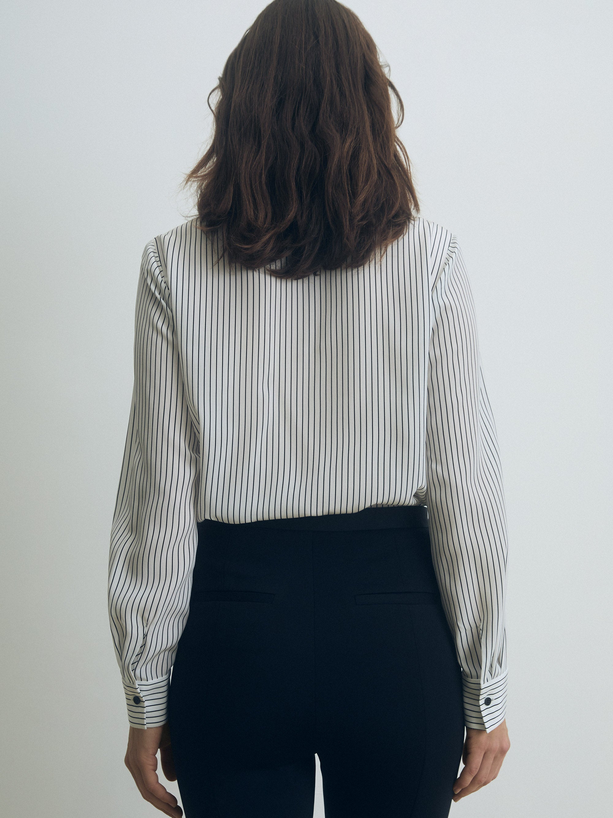 Person wearing a striped shirt and black pants against a white background