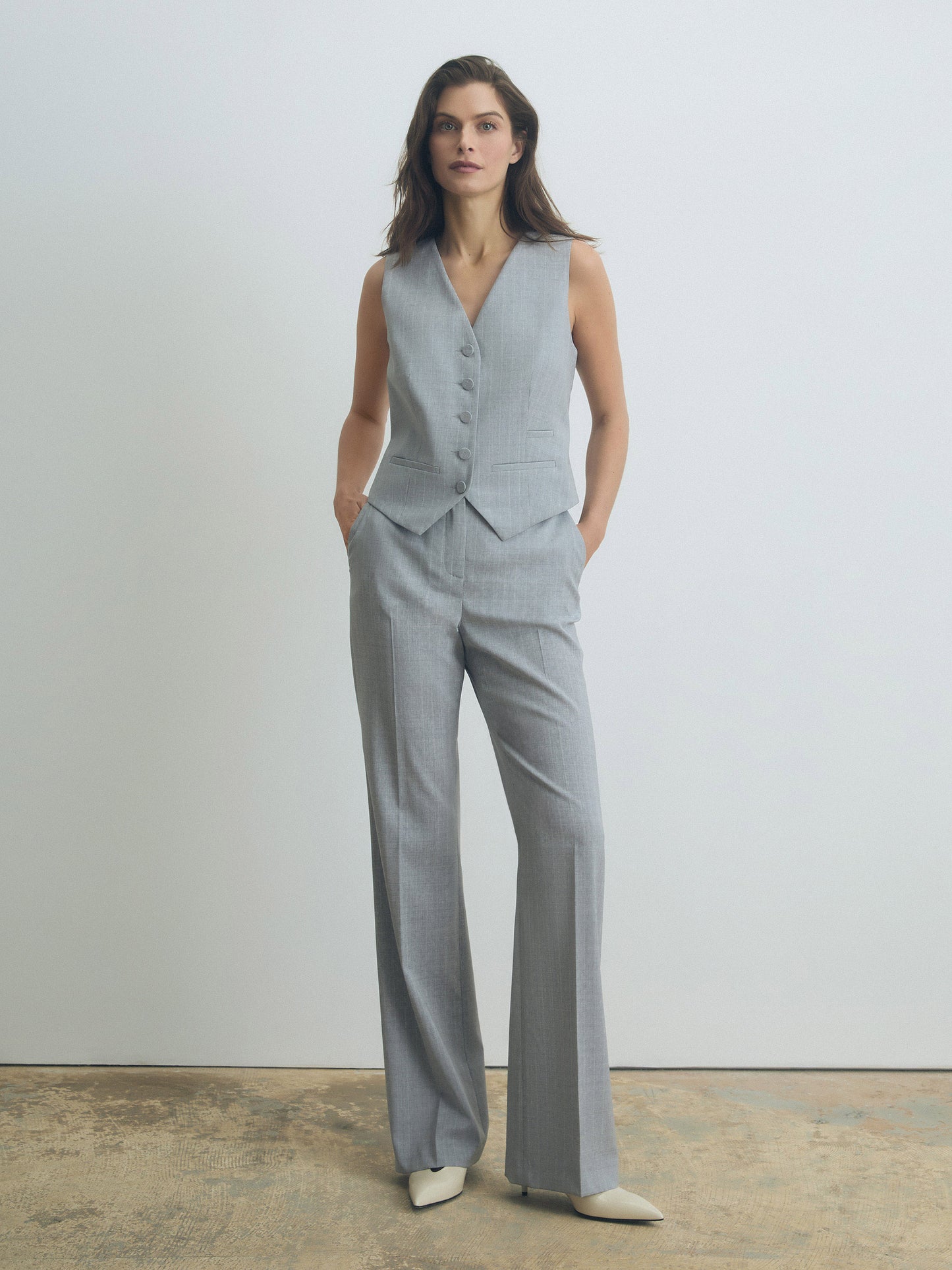 Woman wearing a gray vest and pants set against a plain background