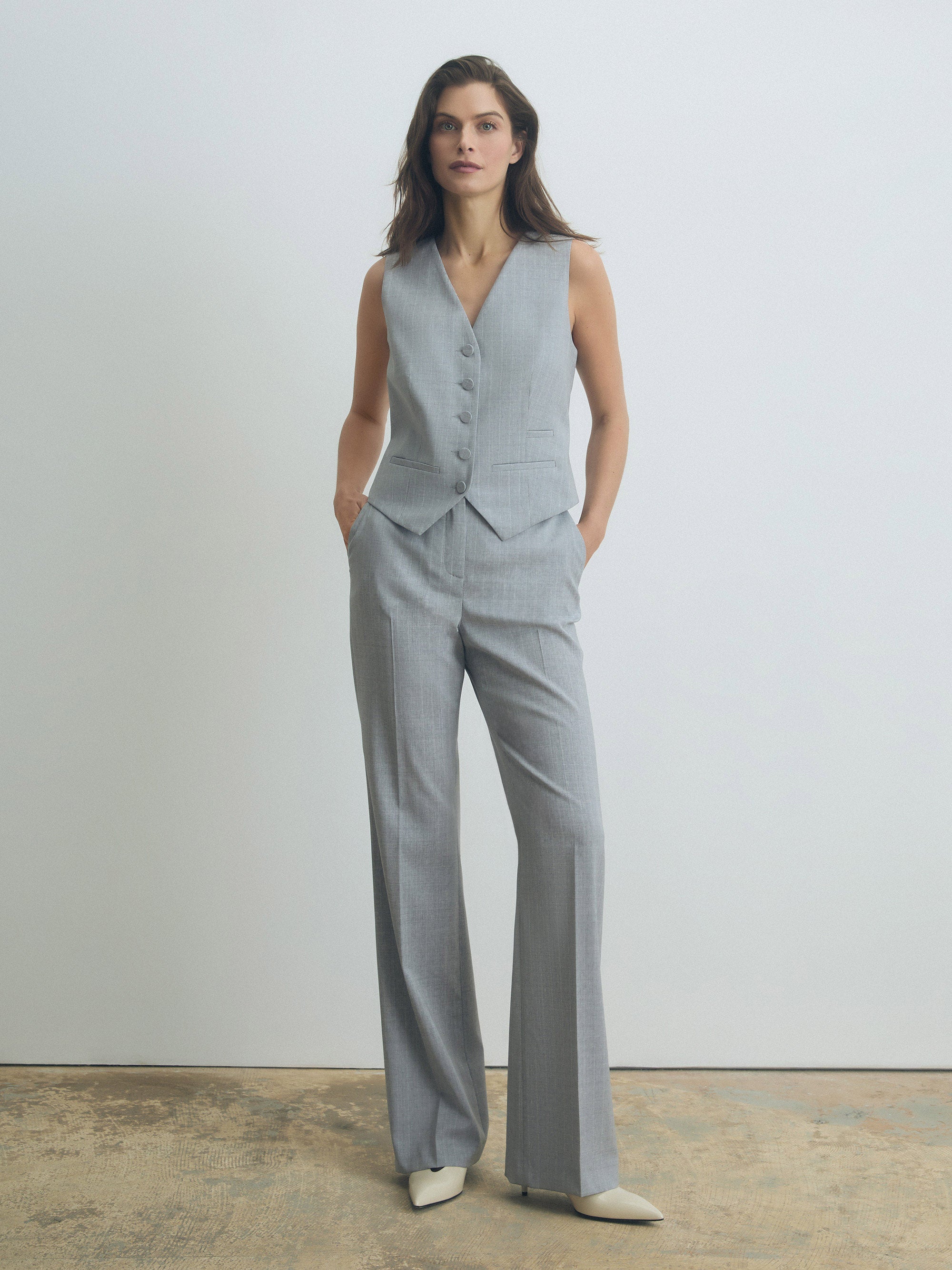 Woman wearing a gray vest and pants set against a plain background