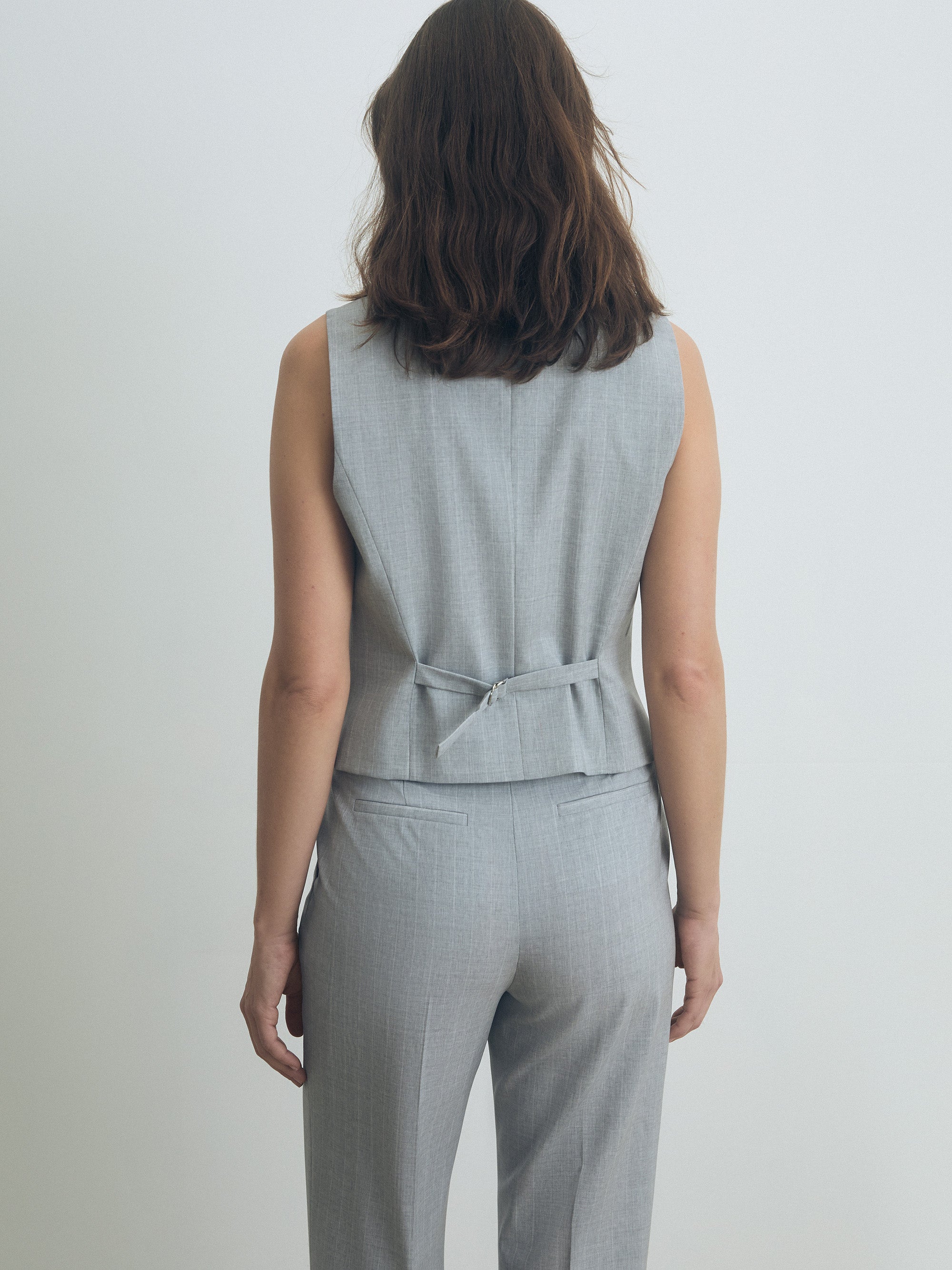 Woman wearing a gray sleeveless vest and pants set on a plain background