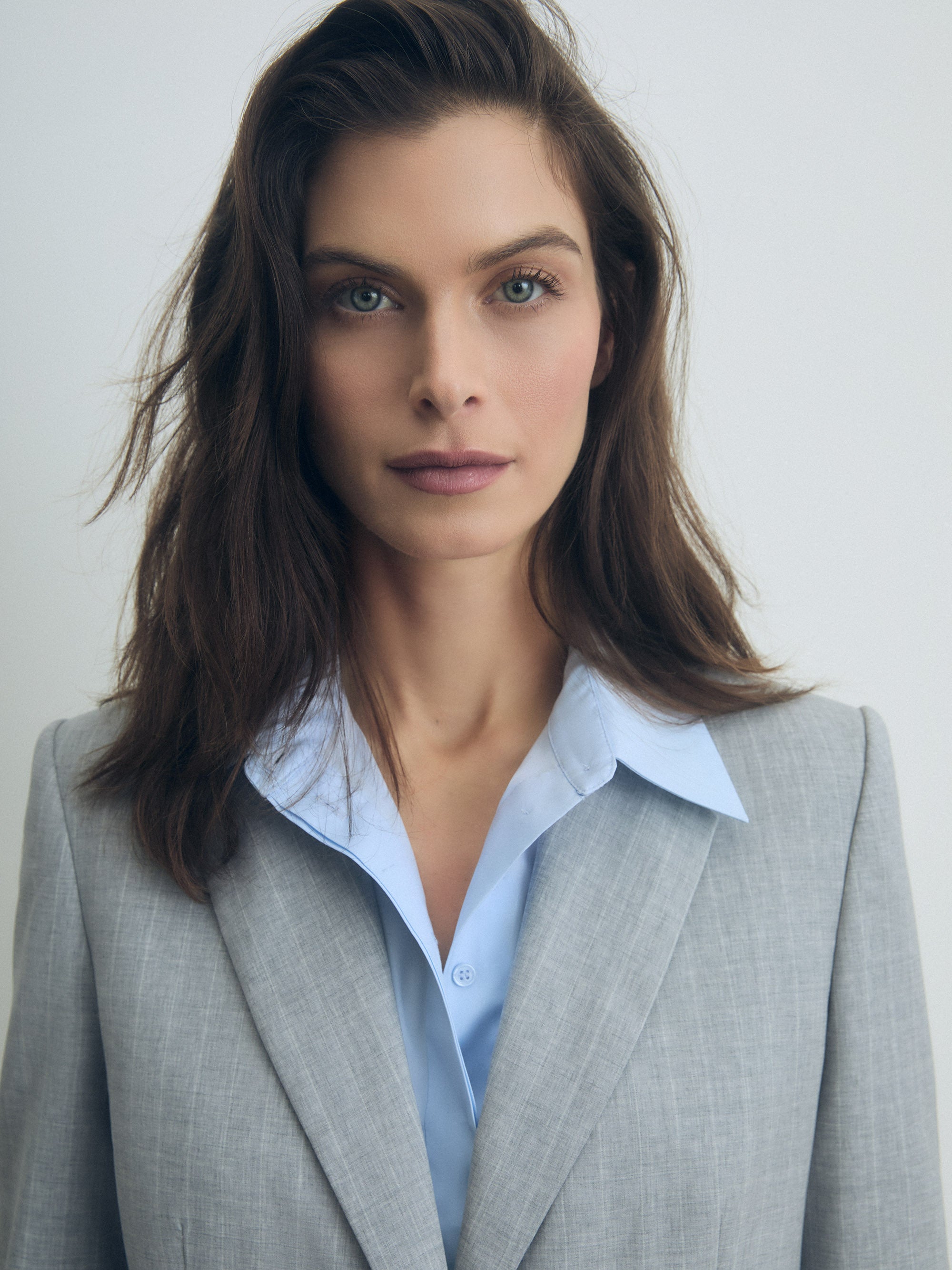 Woman wearing a gray suit and light blue shirt against a plain background