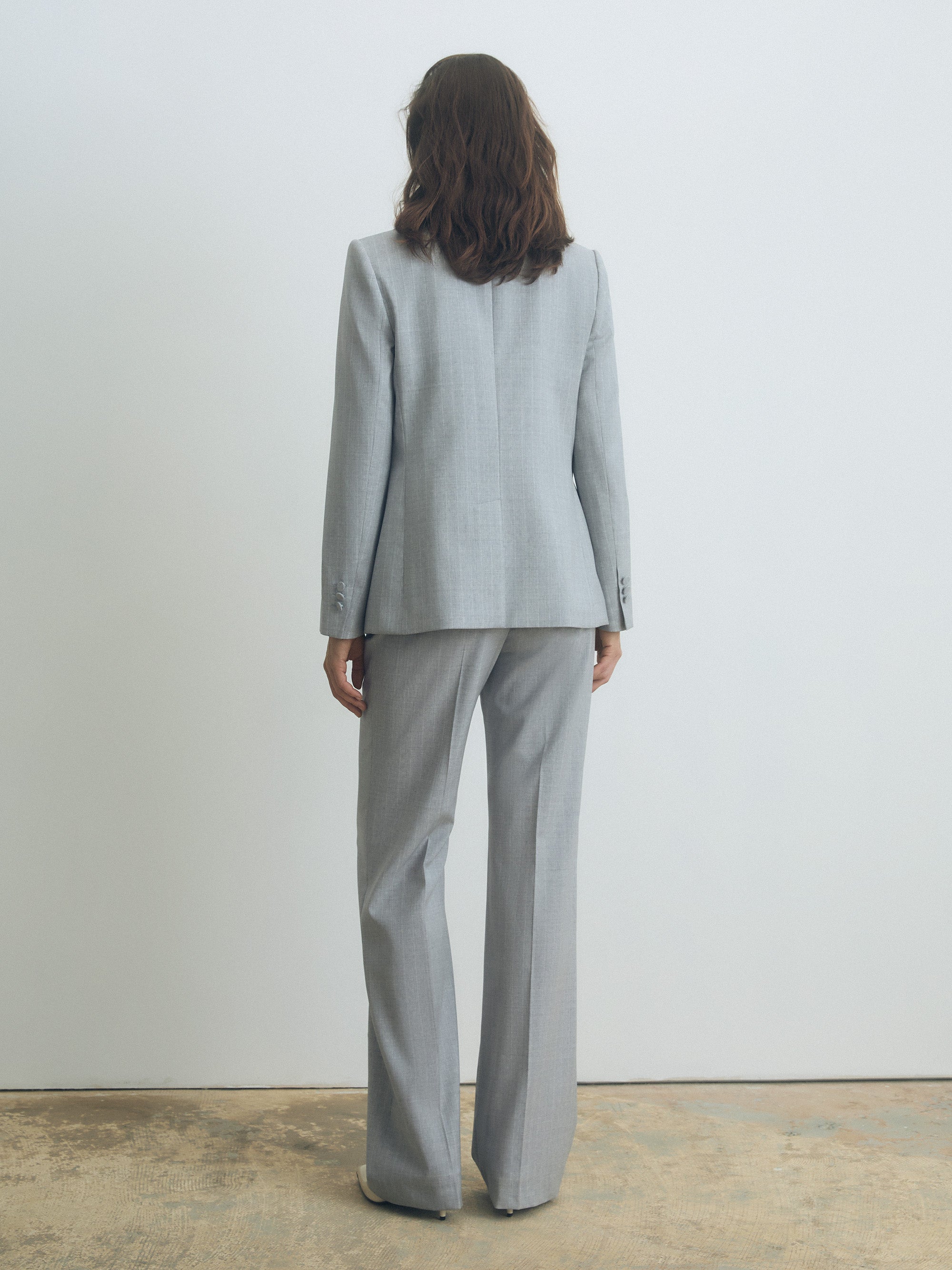 Person wearing a gray stripe suit standing against a plain white wall.