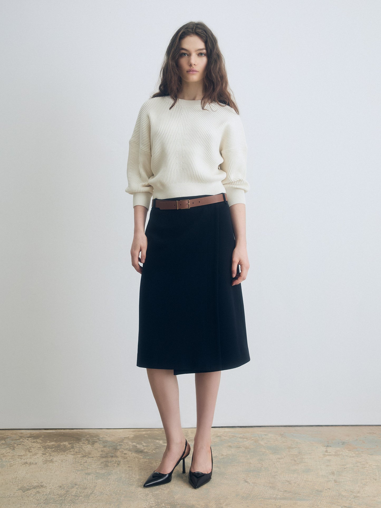 Front view of a navy A‑line skirt styled with a cream ribbed sweater and black pointed‑toe heels.