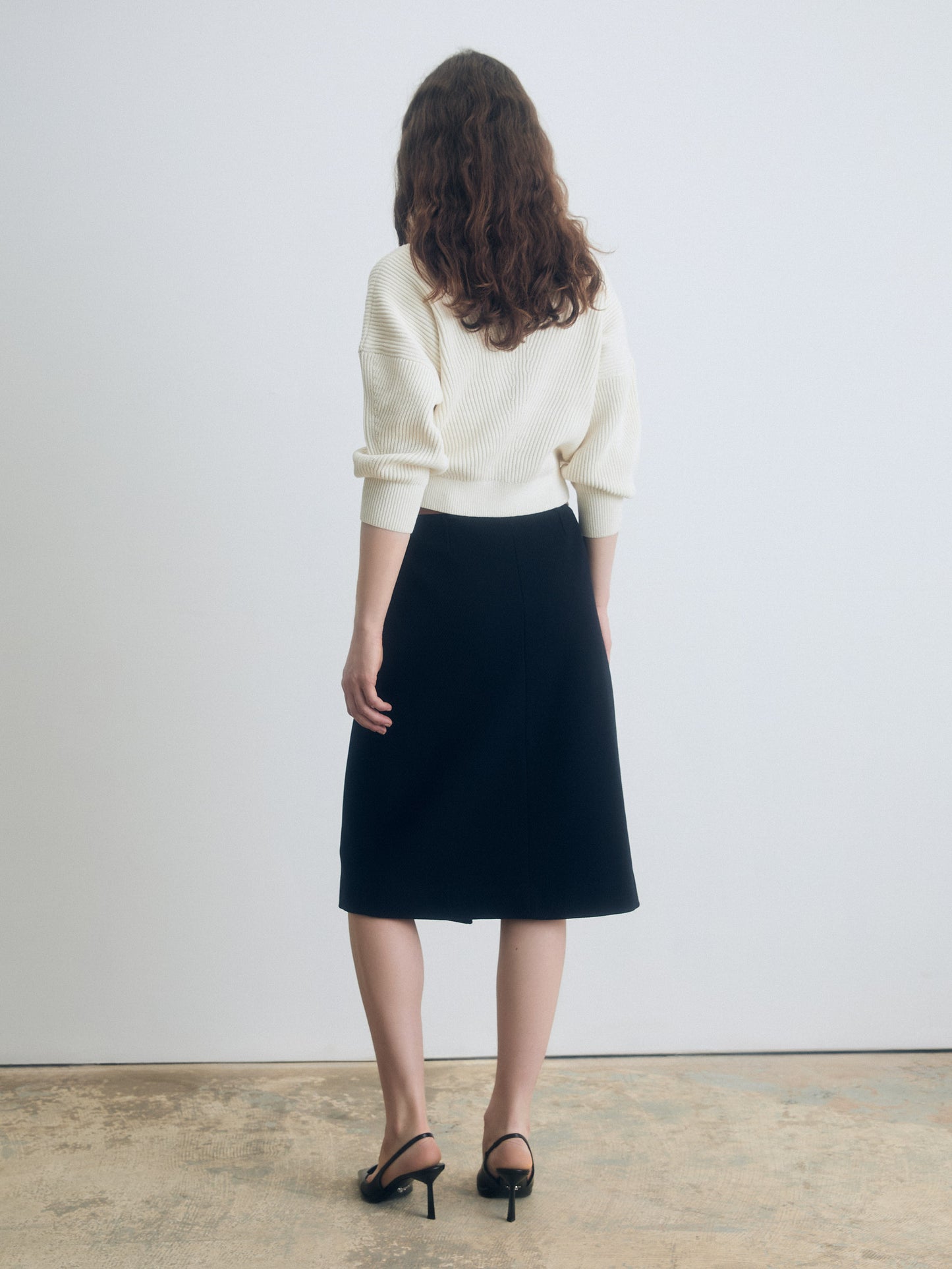 Back view of a navy A‑line skirt styled with a cream knit top and black heeled sandals