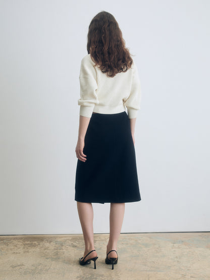 Back view of a navy A‑line skirt styled with a cream knit top and black heeled sandals