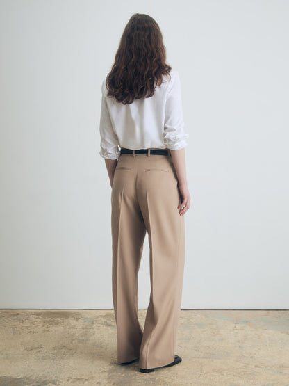 Woman wearing a white shirt and camel pants against a plain background