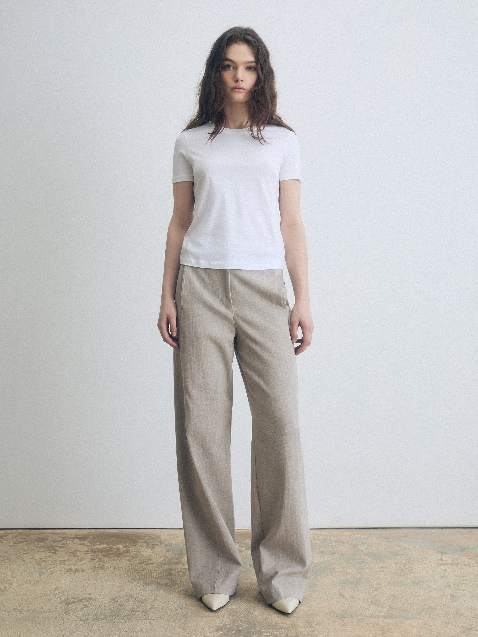Woman wearing a white t-shirt and beige wide-leg pants against a plain background