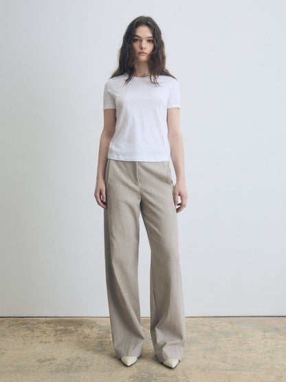 Woman wearing a white t-shirt and beige wide-leg pants against a plain background