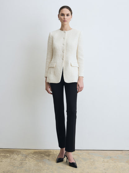 Model wearing a cream textured tweed blazer with a round collar, button‑front closure, and front flap pockets, paired with slim black pants and black heels, standing against a light grey background.