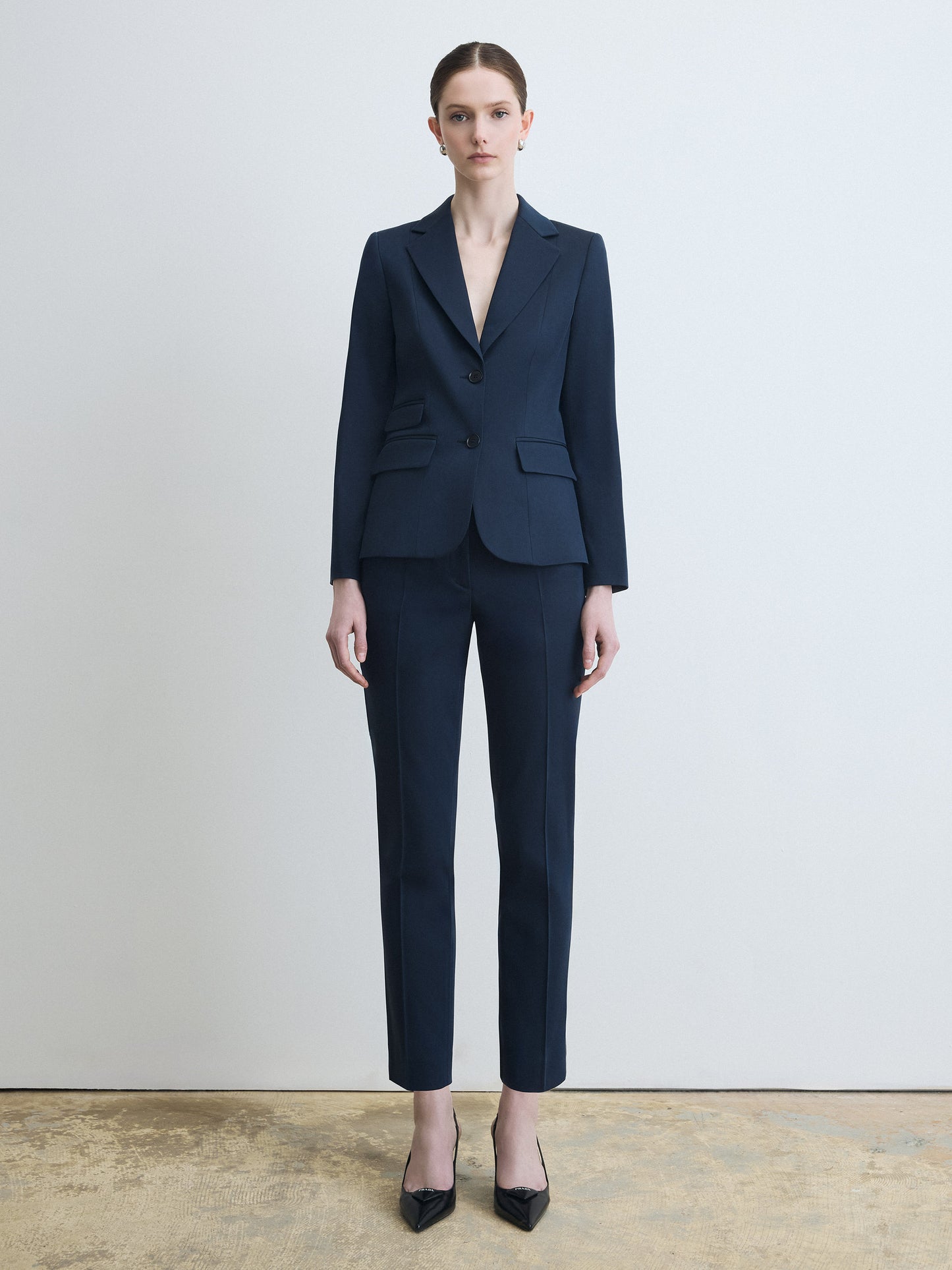 Person wearing a navy blue suit standing against a plain background