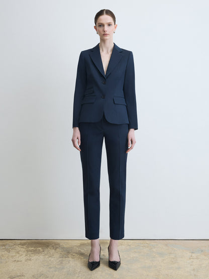 Person wearing a navy blue suit standing against a plain background