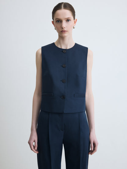 Woman wearing a navy blue sleeveless vest and pants on a light gray background