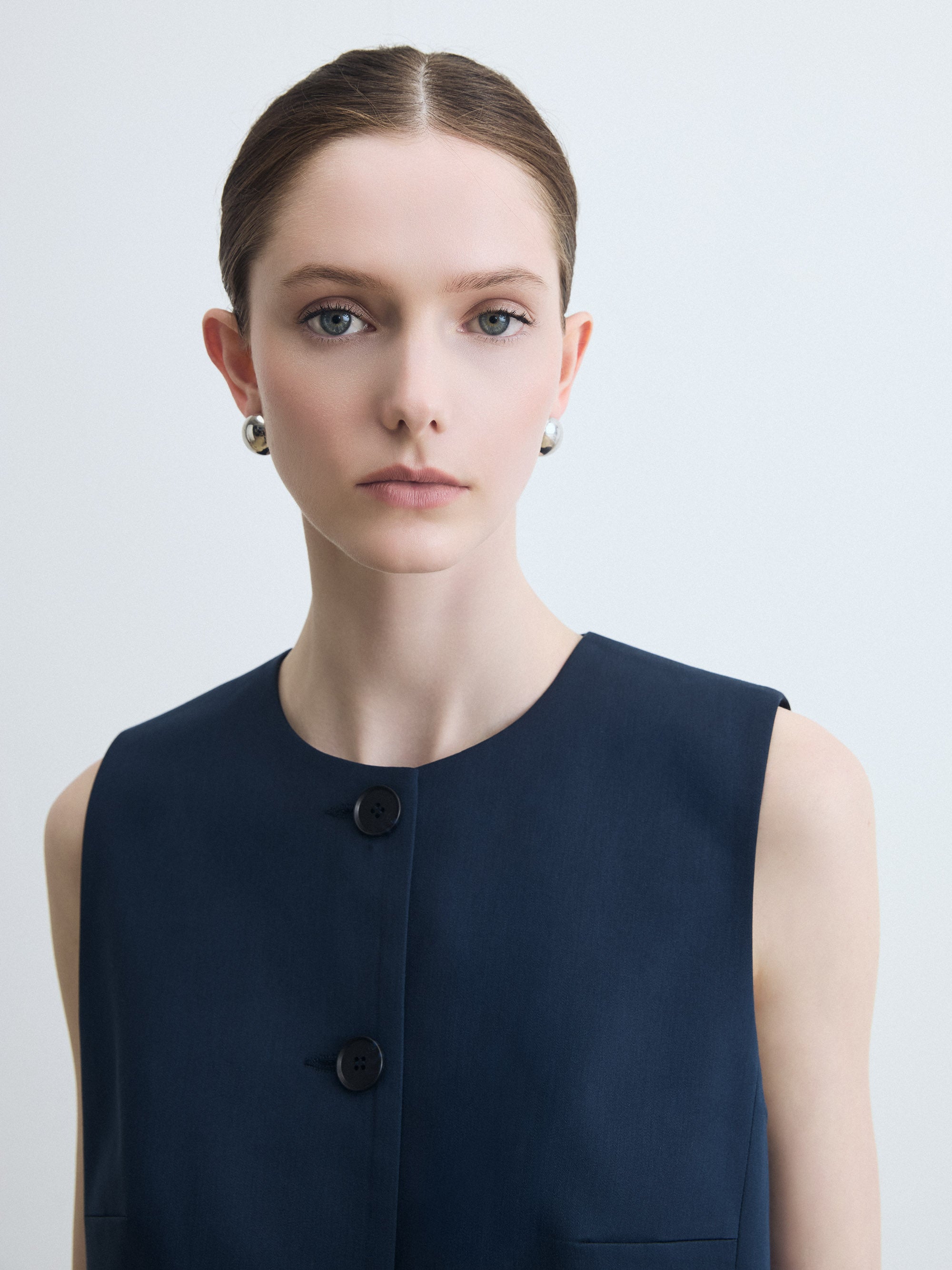 Woman wearing a navy sleeveless vest with buttons on a light gray background