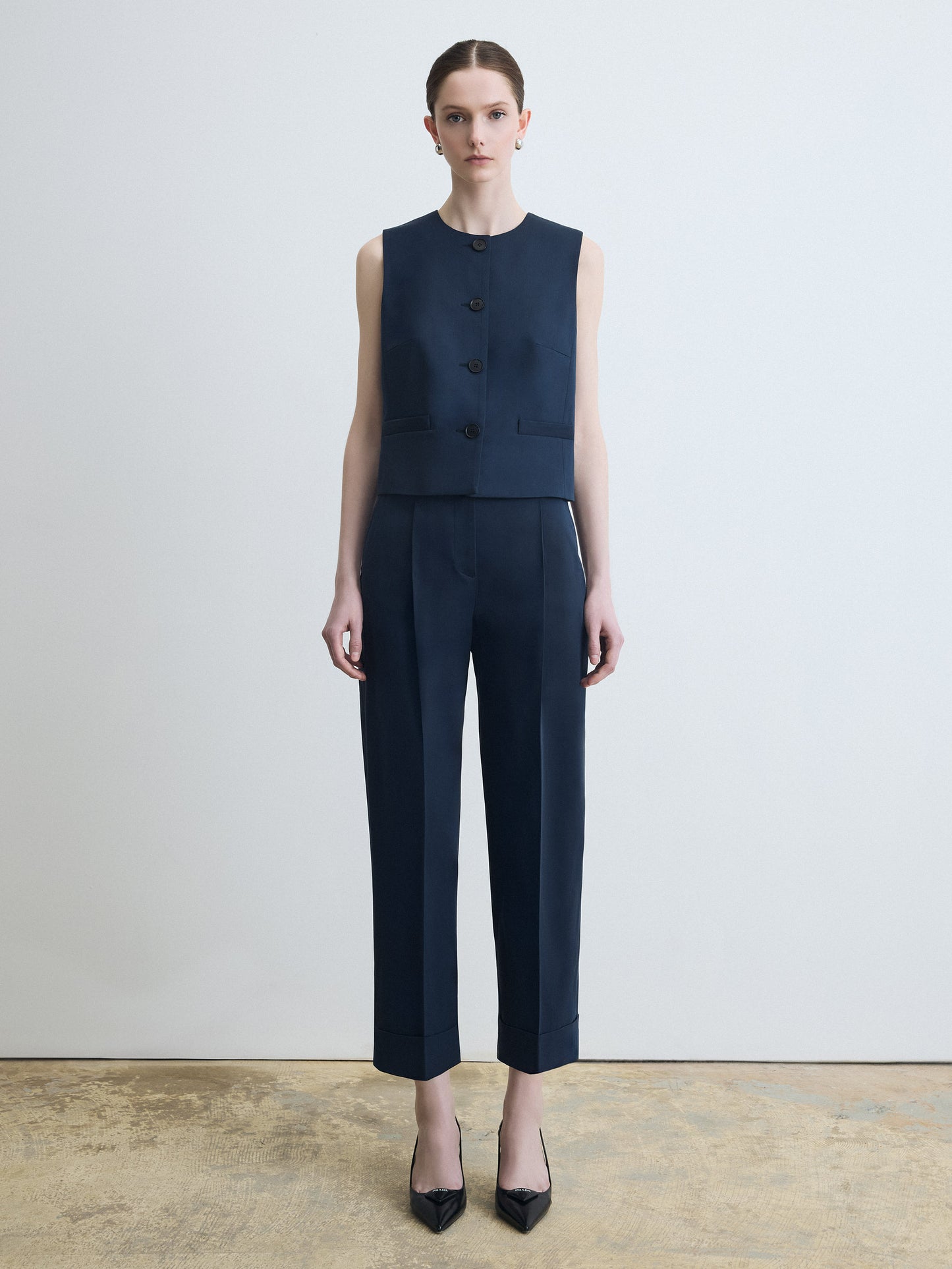 Woman wearing a navy sleeveless top and pants against a white background