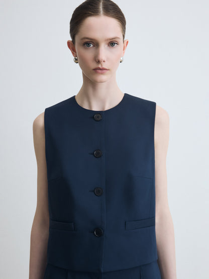 Woman wearing a navy blue sleeveless vest with buttons on a light gray background