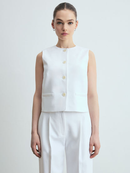 Woman wearing a white sleeveless top with buttons on a plain background