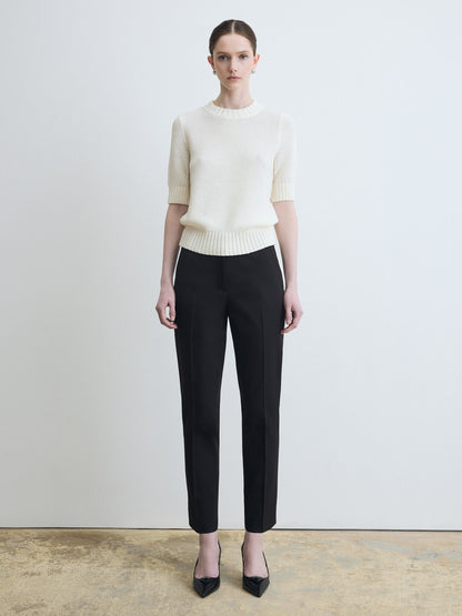 Woman wearing a white sweater and black pants against a plain background