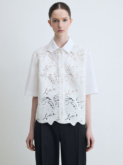 Woman wearing a white lace blouse with black pants on a plain background