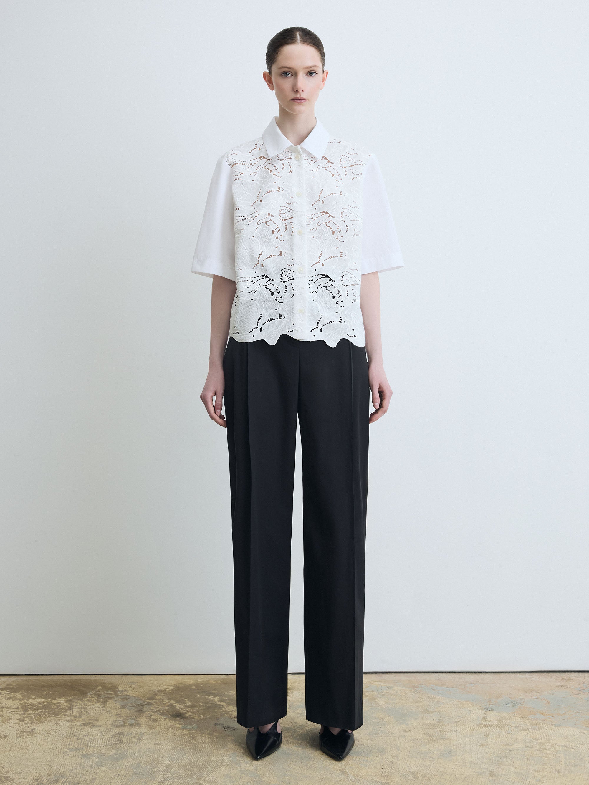 Person wearing a white lace blouse and black pants against a plain background