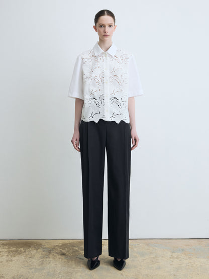 Person wearing a white lace blouse and black pants against a plain background