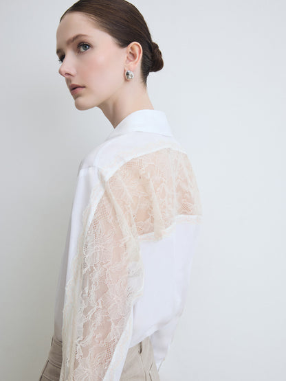Woman wearing a white blouse with lace detailing on a plain background