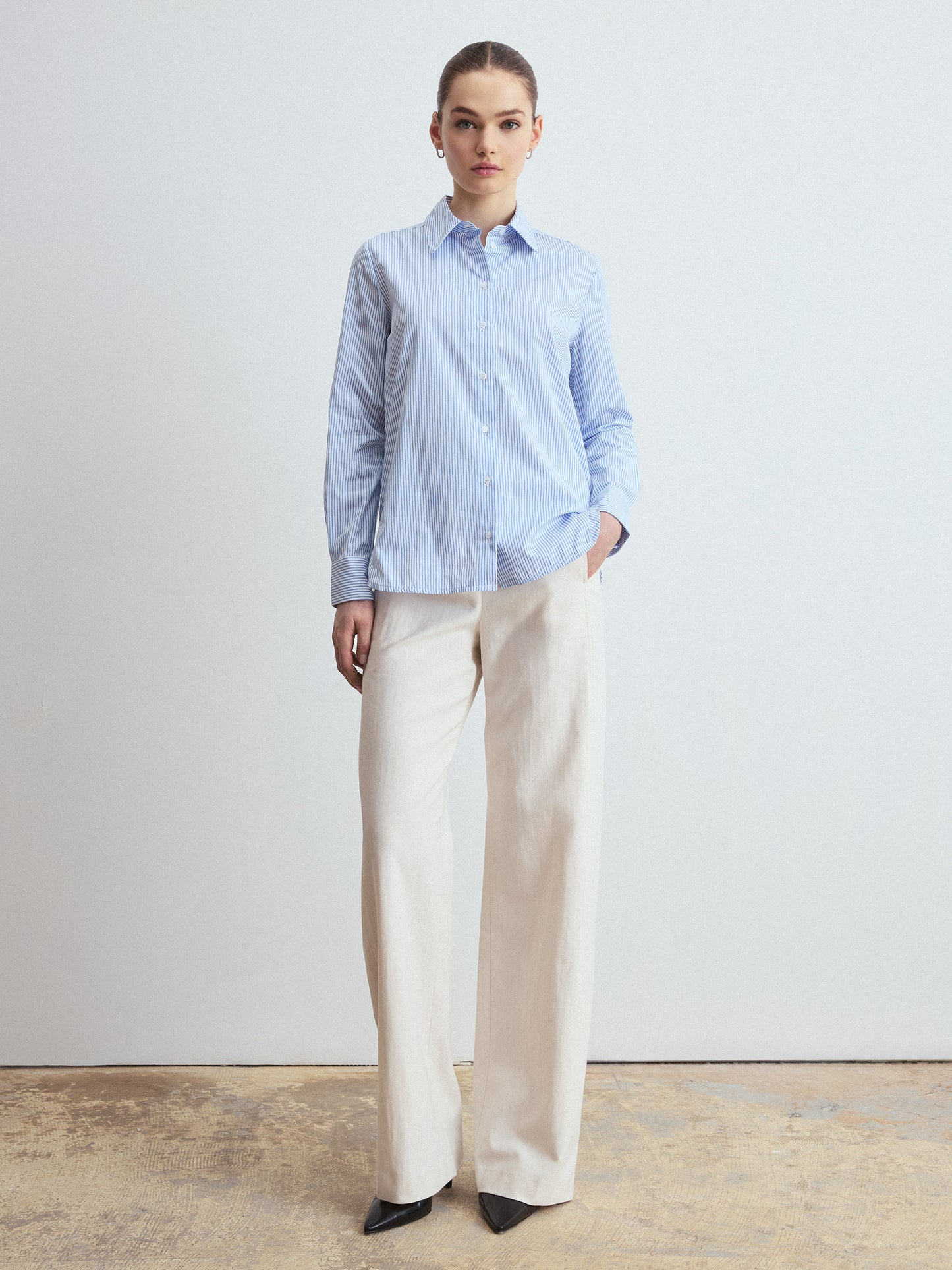 Person wearing a light blue striped shirt and beige pants against a plain background