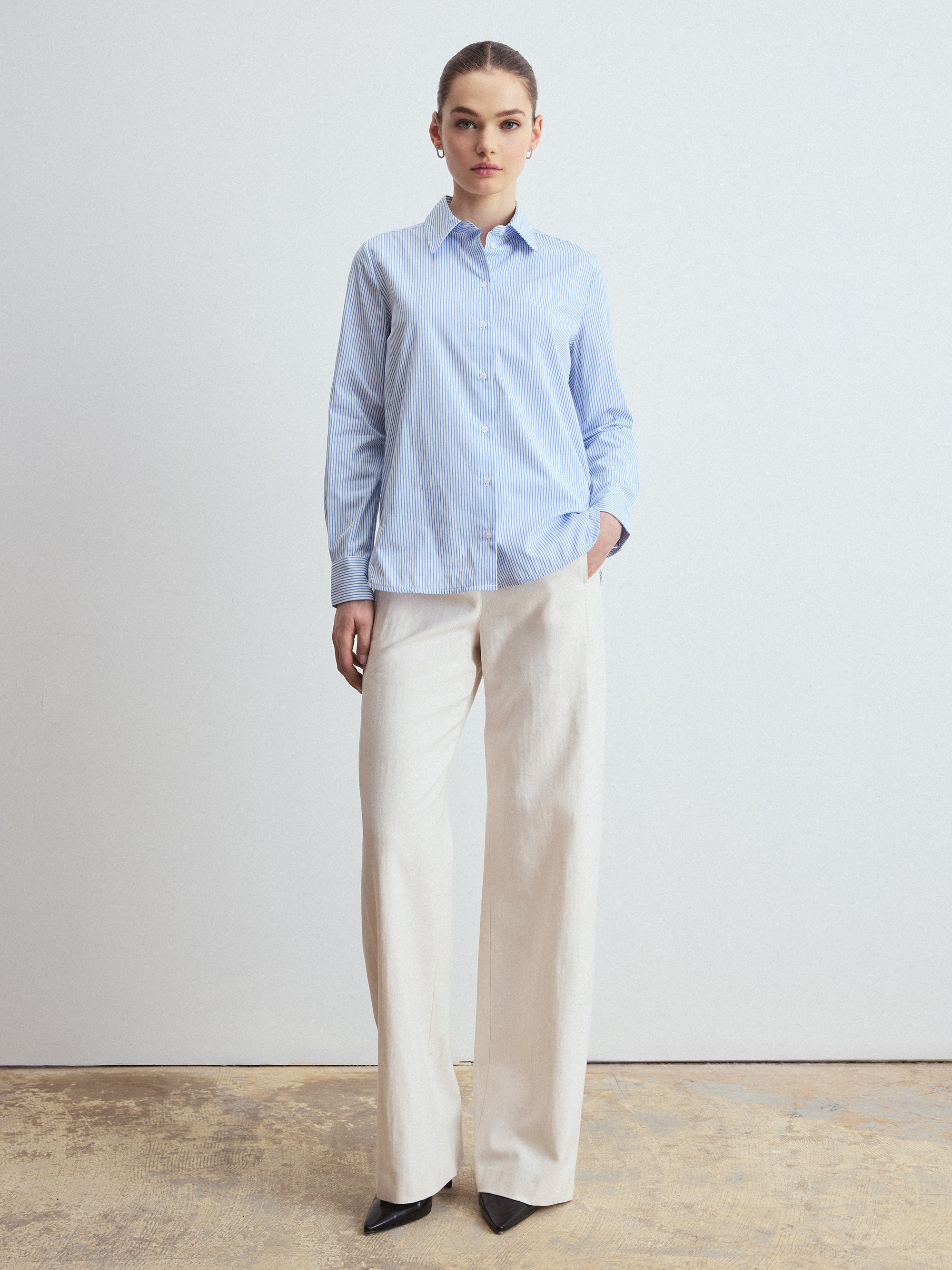 Person wearing a light blue striped shirt and beige pants against a plain background