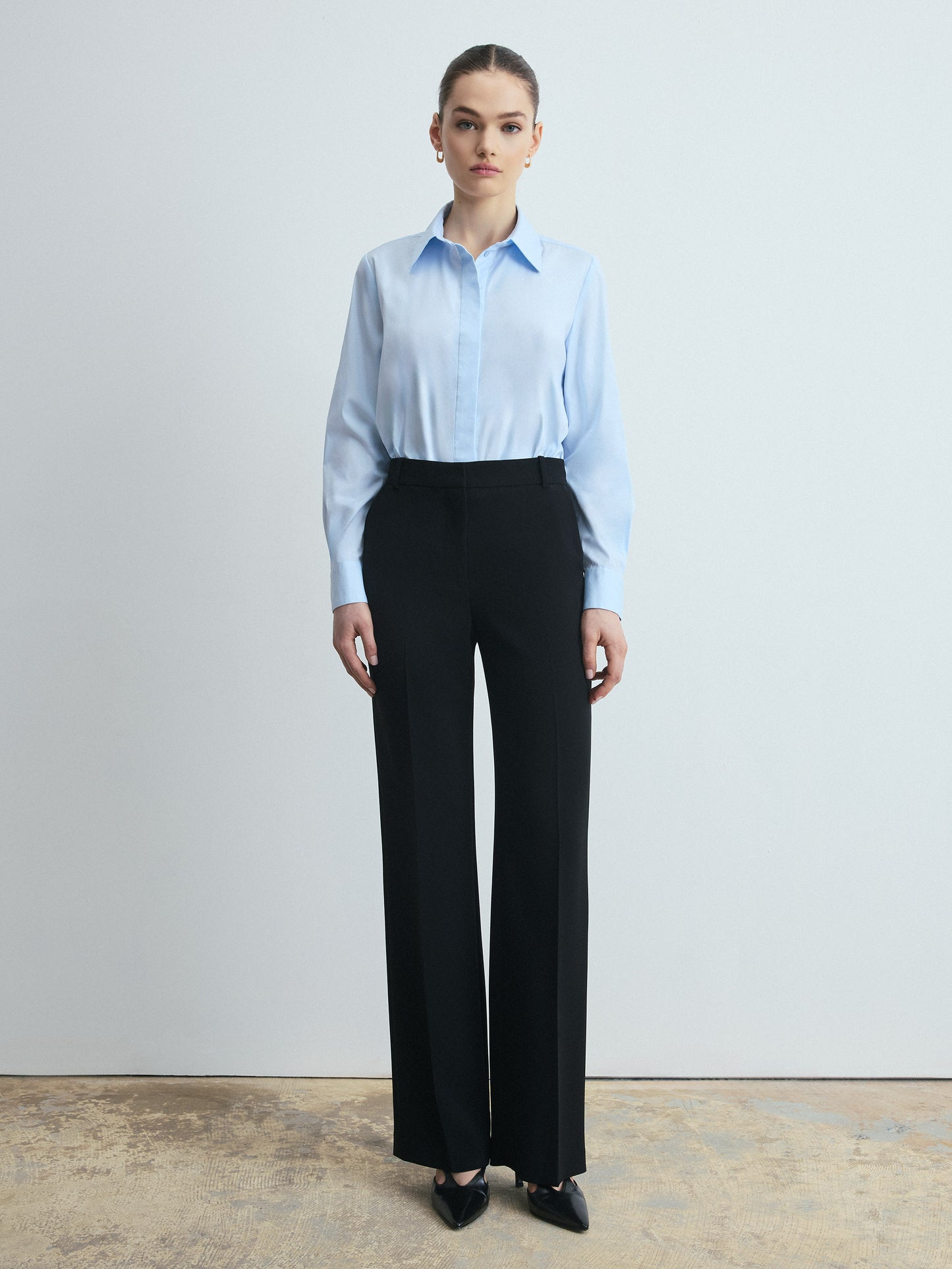 Person wearing a light blue shirt and black pants against a plain background