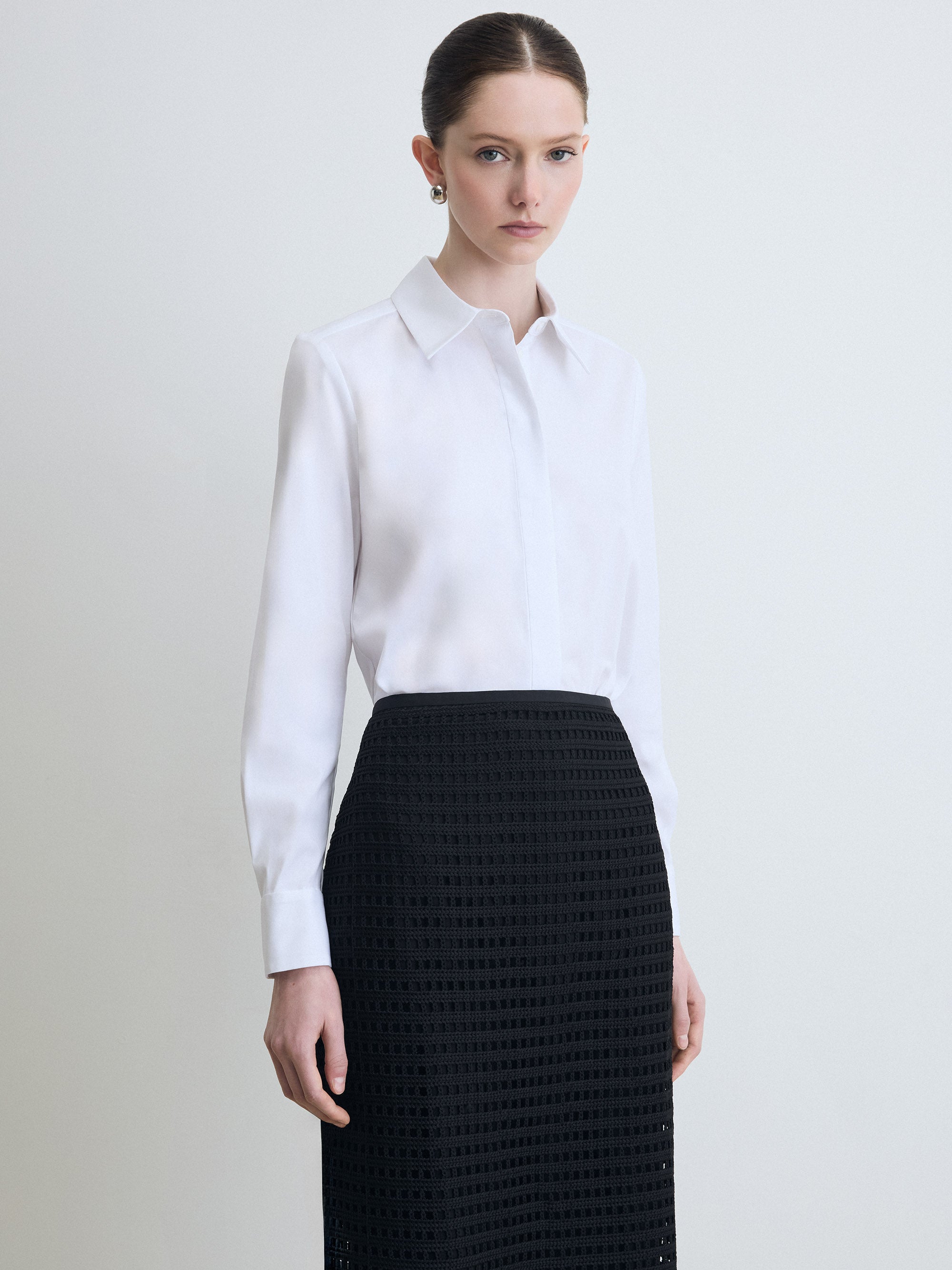 Person wearing a white shirt and black skirt against a plain background