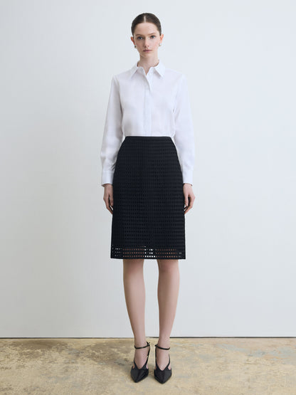 Person wearing a white shirt and black patterned skirt on a plain background