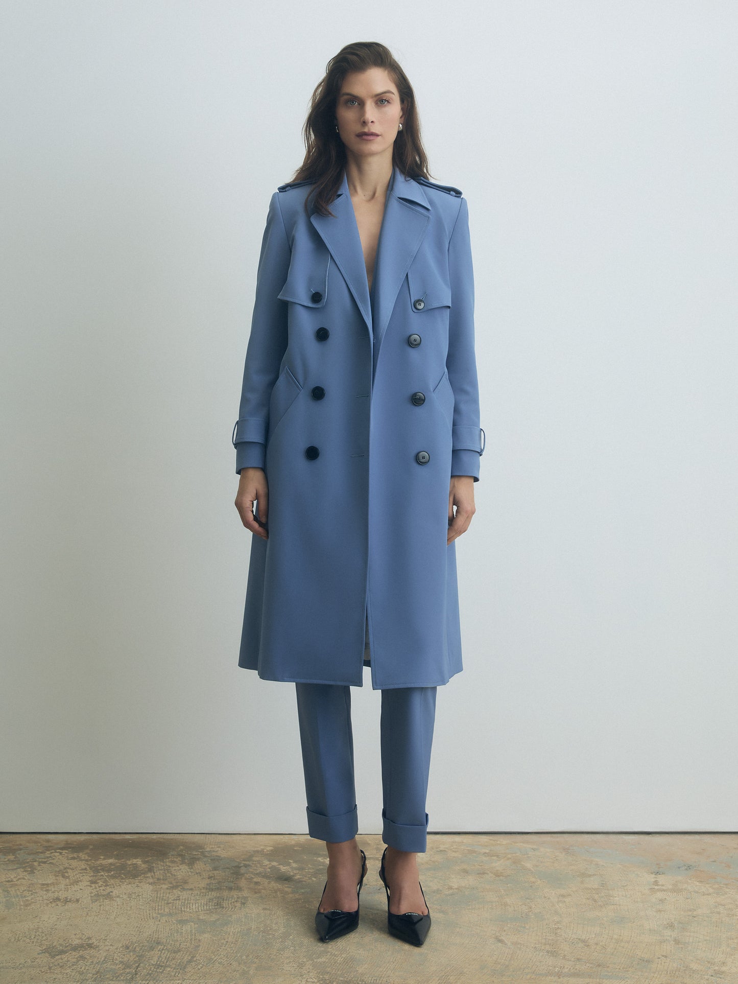Woman wearing a blue trench coat and pants on a plain background