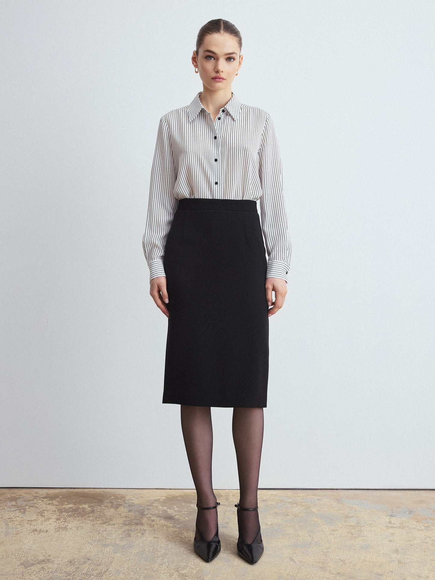 Woman wearing a striped shirt and black skirt against a plain background