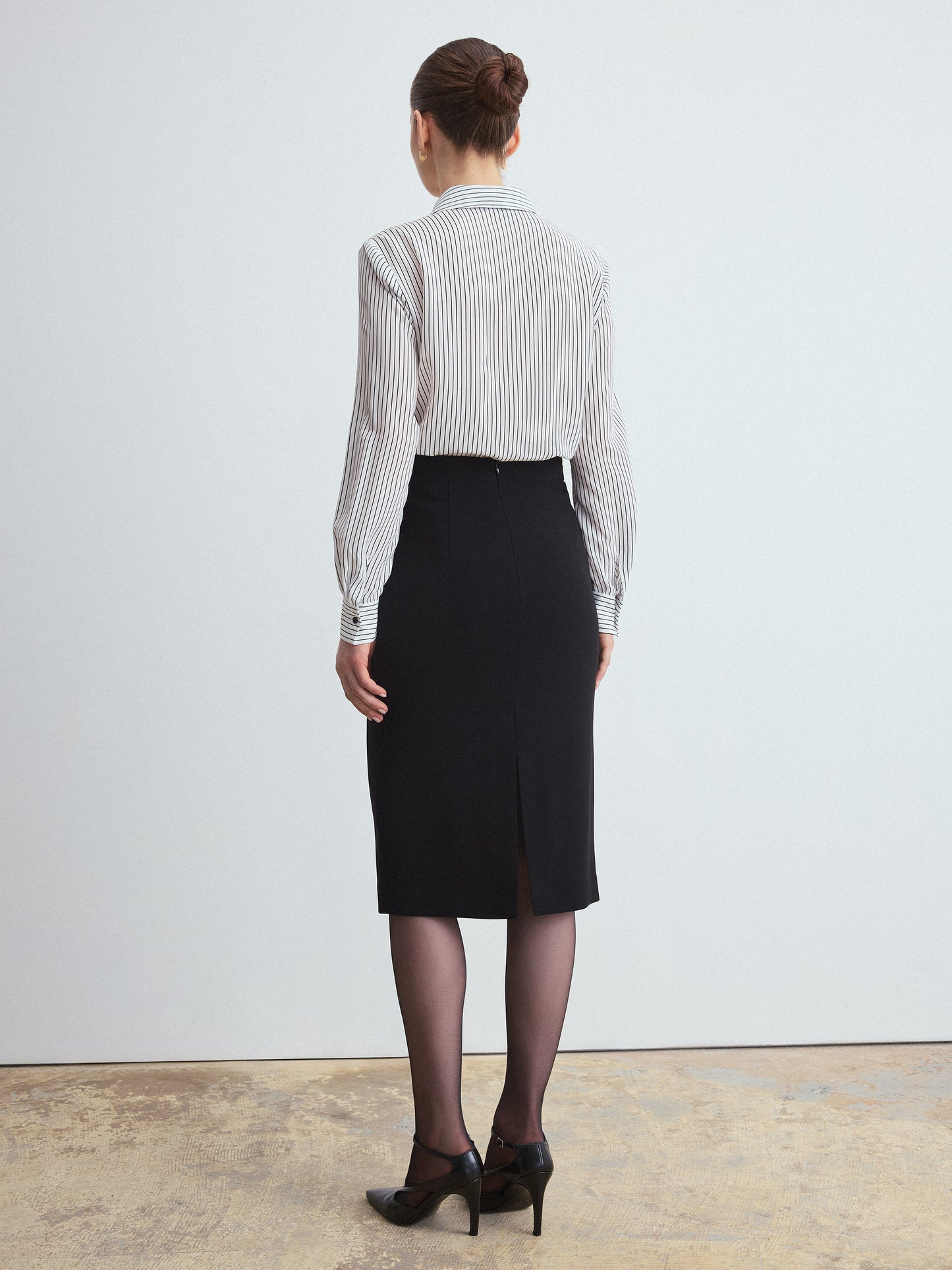 Person wearing a striped shirt and black skirt against a white background