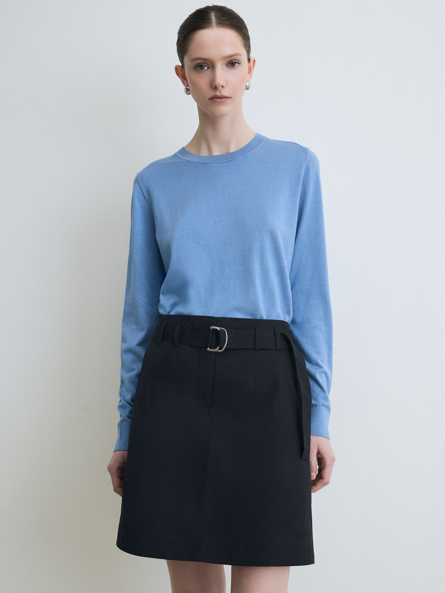 Woman wearing a light blue sweater and black skirt on a plain background