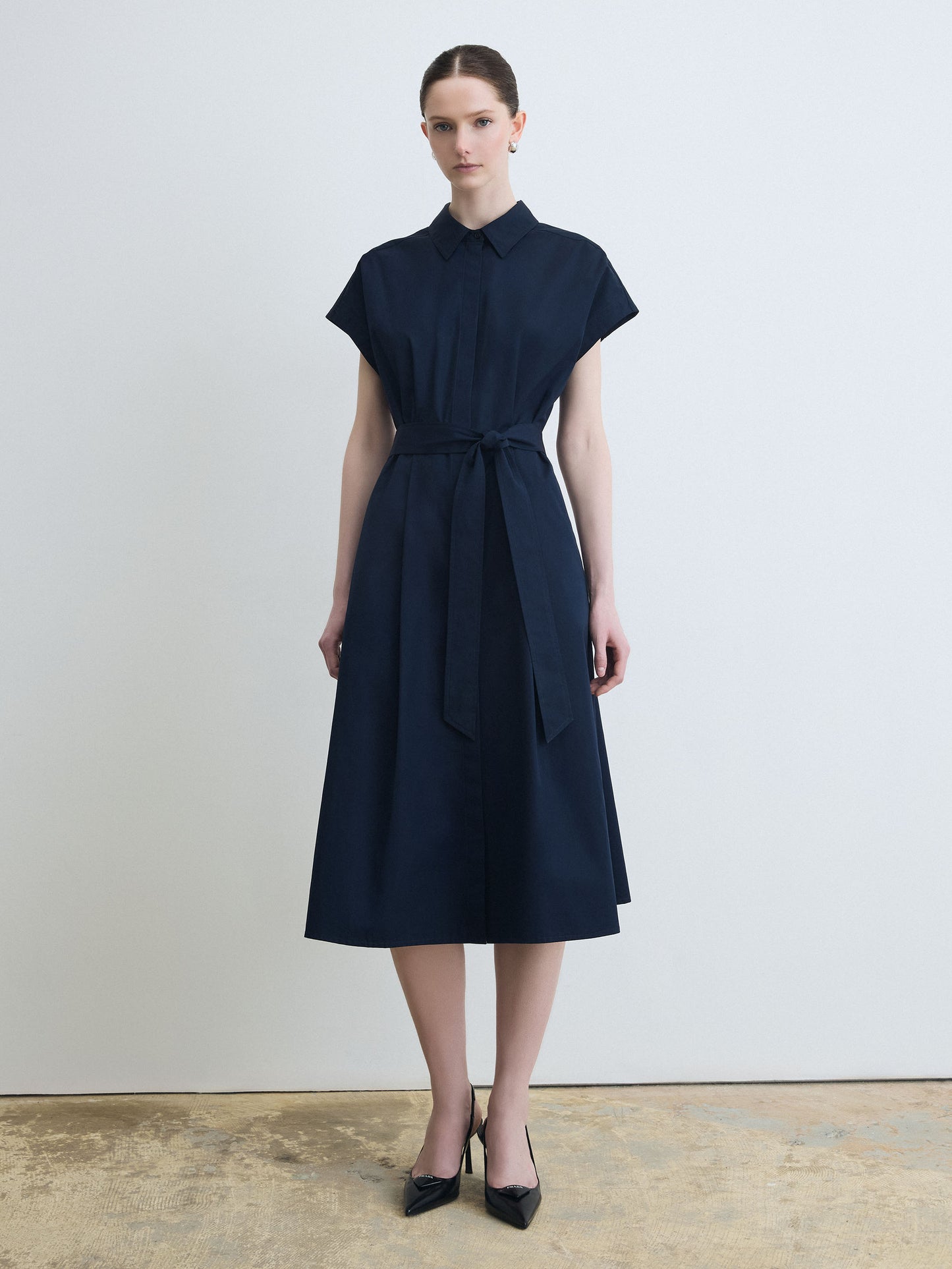 Woman wearing a navy dress with a belt against a plain background