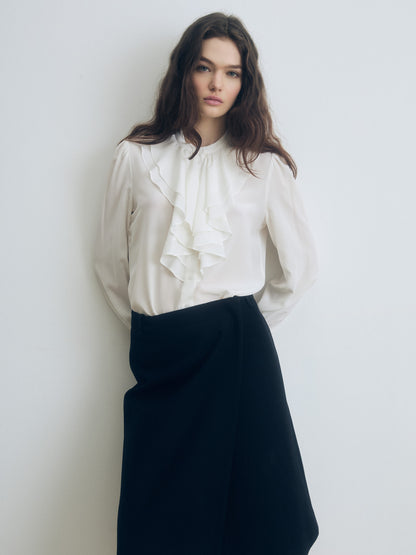 Woman wearing a white blouse with ruffles and a black skirt against a plain background