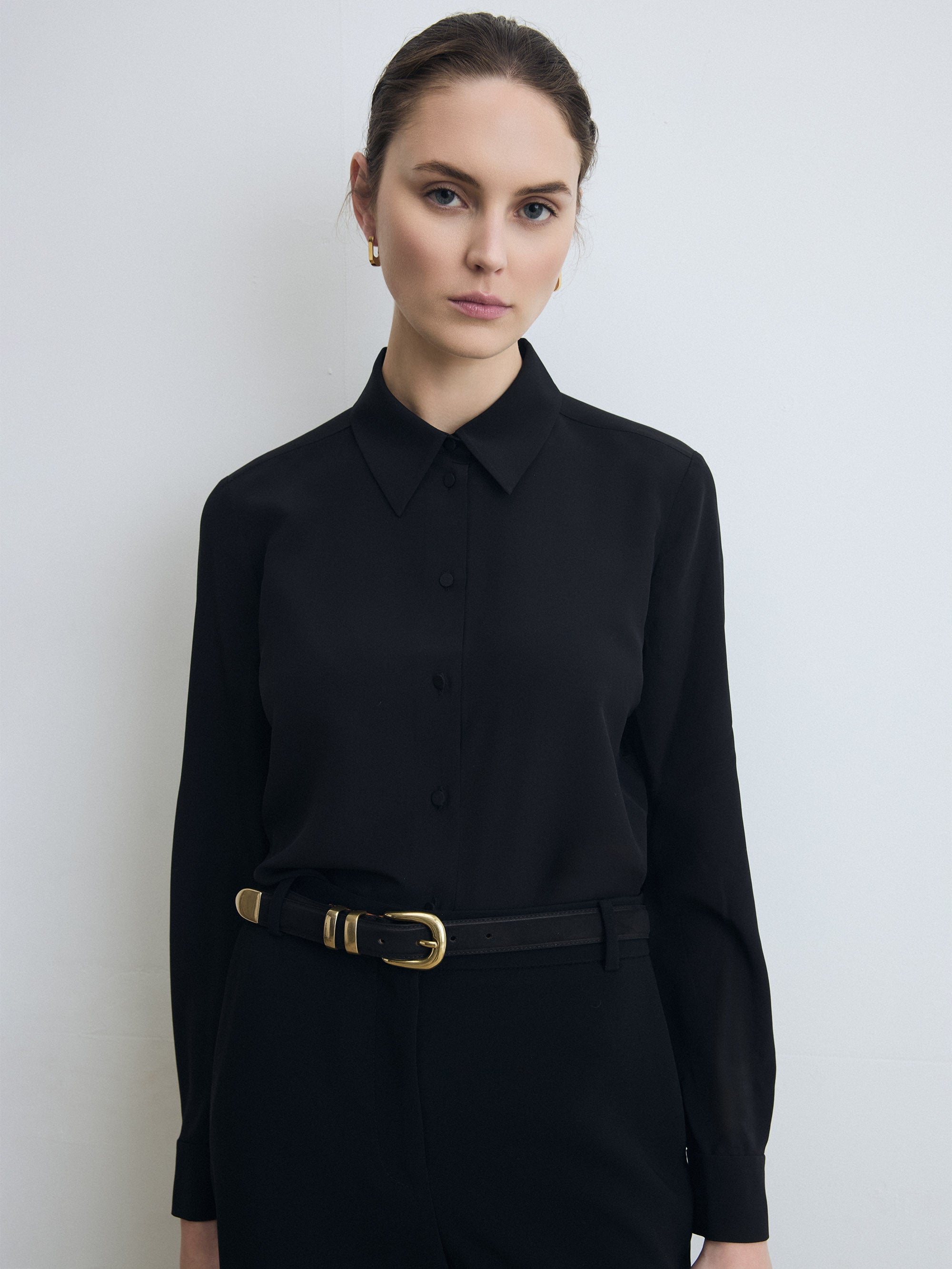 Woman wearing a black blouse with a gold belt against a white background