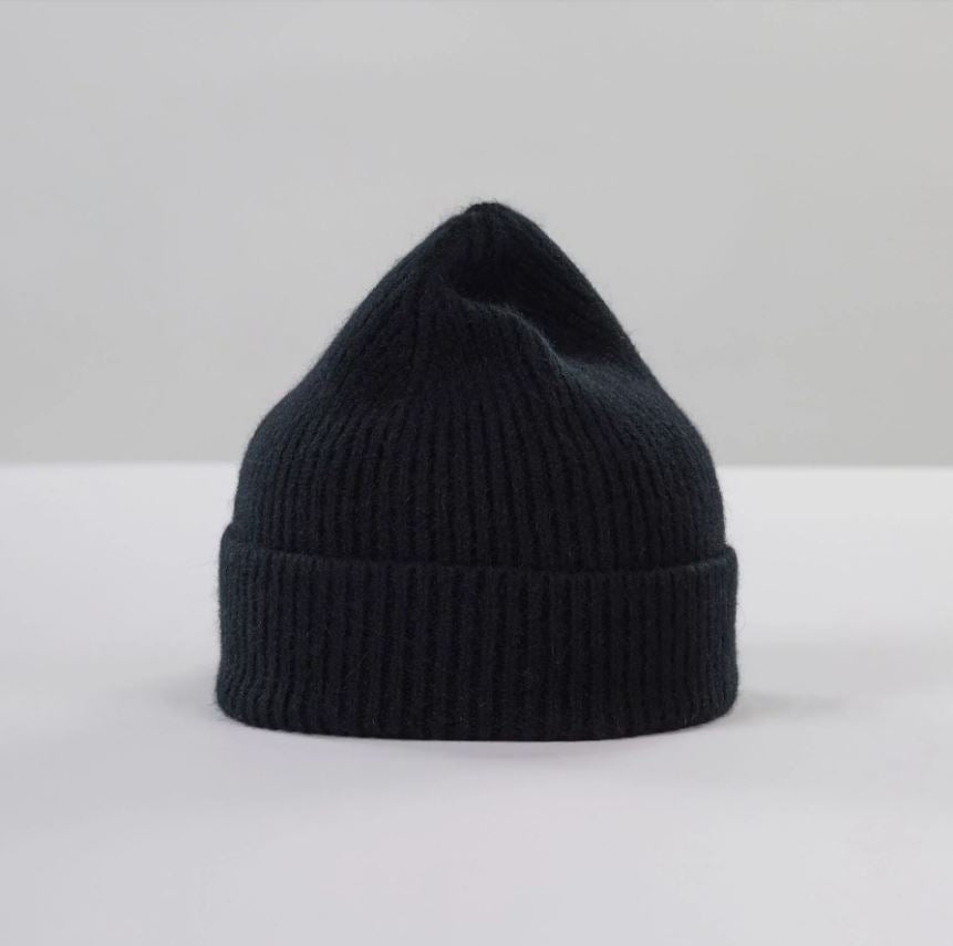 Flat lay of ribbed black beanie in soft lambswool and Caregora blend, classic silhouette in wool knit, made in Scotland
