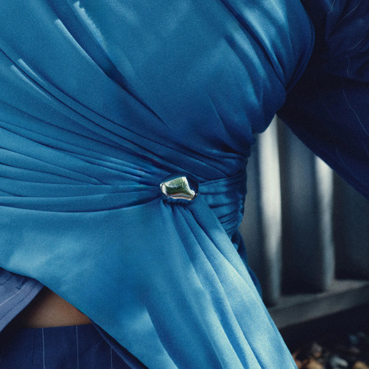 Close-up of a blue dress with a decorative brooch detail.